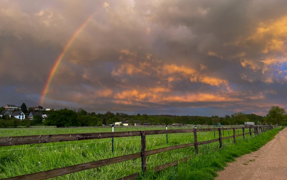 Dieses Bild zeigt einen Regenbogen vor einem von der Abendsonne angestrahltem Himmel. Die Wolken leuchten durch den Sonnenuntergang in einem schönen rot/orangenen Ton.